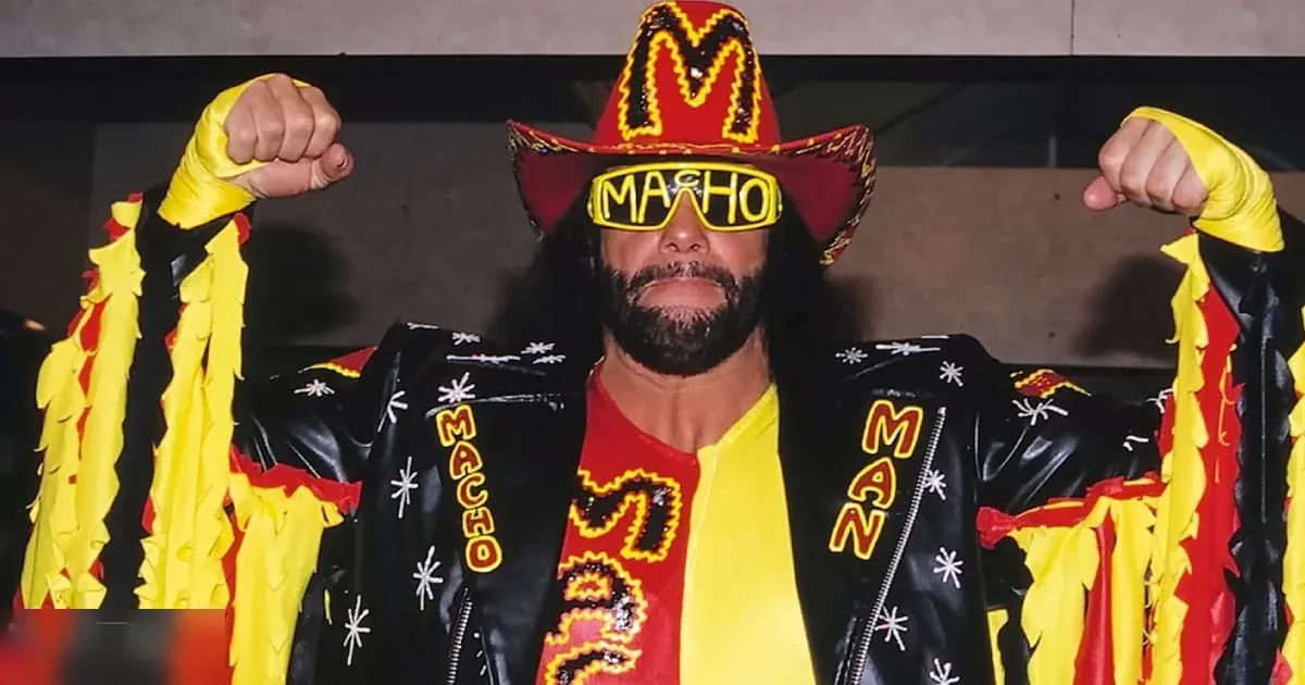 Adult male wrestler wearing a black leather jacket with fringe details, sequined stars on shoulders, 'MACHO MAN' text on sleeves, red and yellow sombrero, sunglasses, wrist wraps. Indoor wrestling arena setting.
