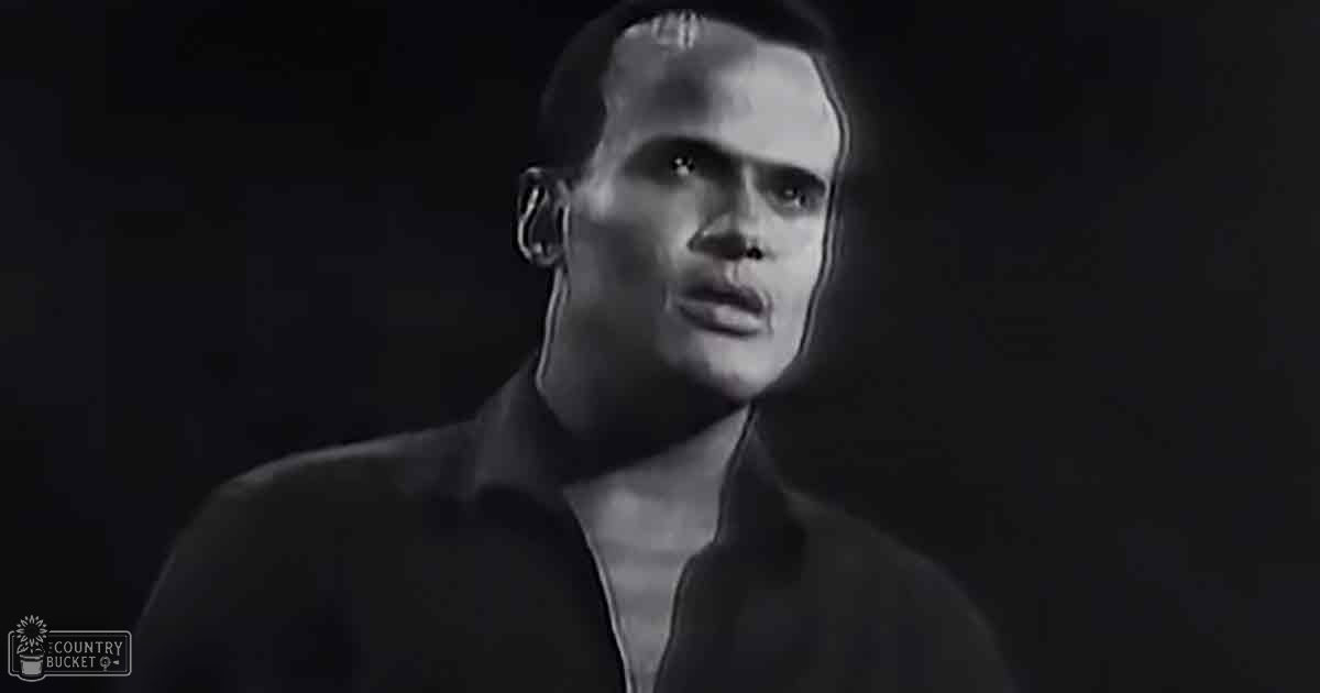A young adult male in a relaxed, modern casual shirt with long sleeves and a high collar stands indoors against a plain dark background.