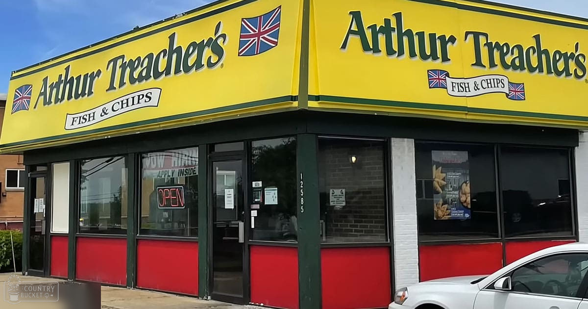 Arthur Treacher's Fish & Chips restaurant exterior with 'Now Hiring' and 'Open' signs displayed on large windows during daytime under clear skies, yellow signage, red building lower part, green window trim.
