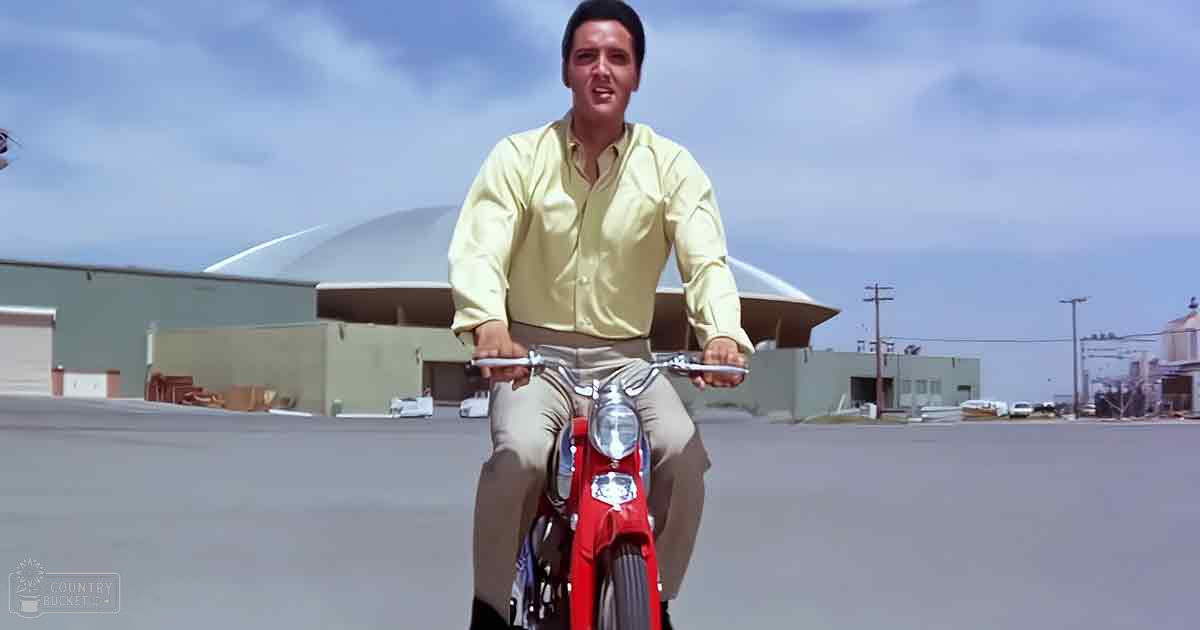 Adult male riding a motorcycle in an industrial area with modern buildings, late afternoon lighting.