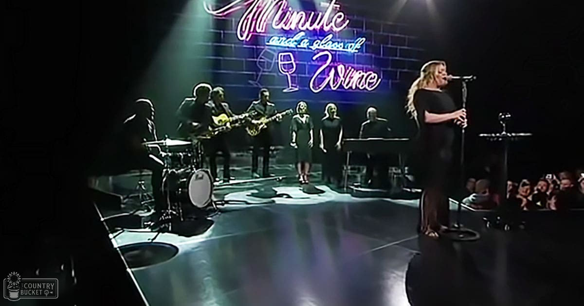 An indoor musical performance with a female singer in a black dress, accompanied by musicians wearing dark attire; vibrant neon signage adds color to the brick-walled venue.