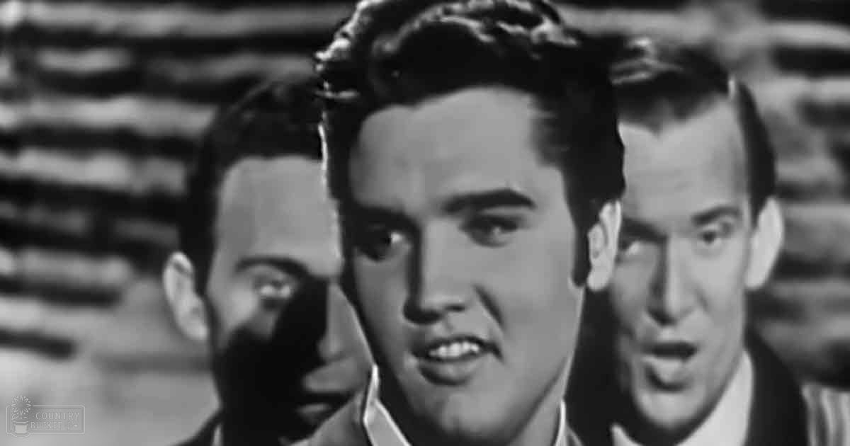 Young adult males wearing dark suits against a brick wall background, possibly part of a performance or scene from a film or television show.