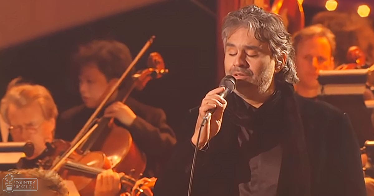 An adult male singer performing in front of an orchestra in a concert hall setting.
