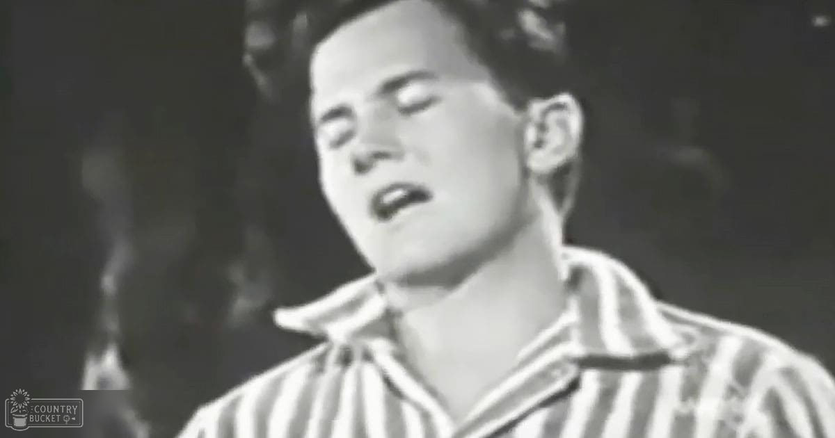 A young adult male in a striped shirt sings into a microphone, set against a dark indoor backdrop with dramatic lighting.