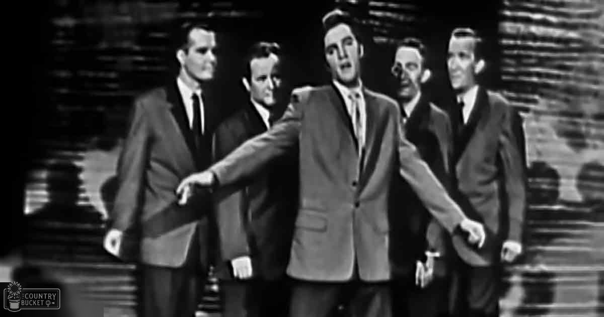 Young adult males in formal suits performing in a studio setting with dark curtains and focused lighting.