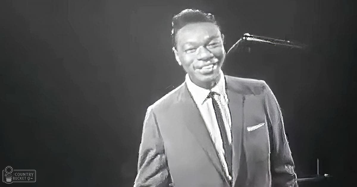A young adult male wearing a formal suit jacket with a pocket square, standing indoors under stage lighting.