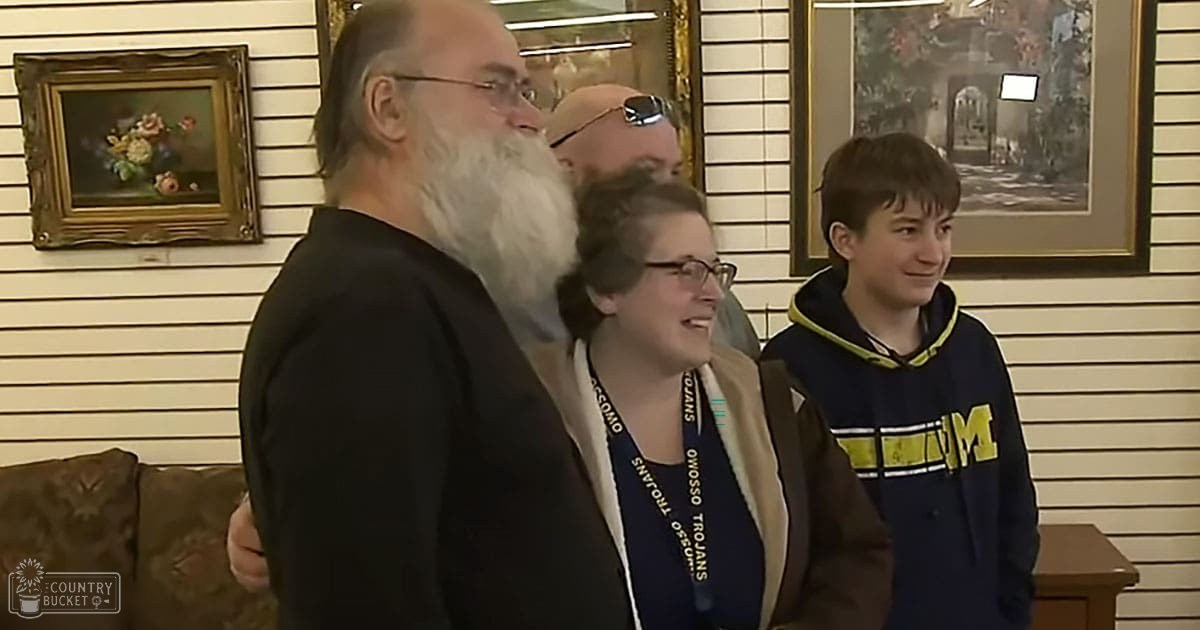 An older adult male wearing glasses and a black shirt indoors with framed artwork, likely in a living room setting.