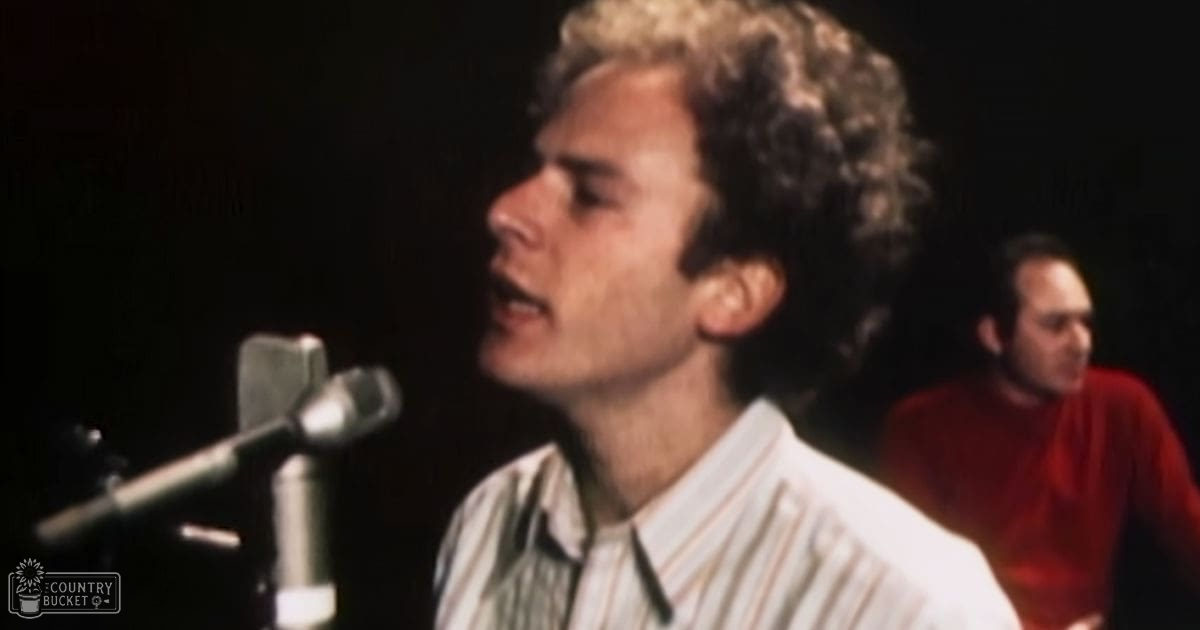 A young adult male singer wearing a white and green striped shirt, holding a microphone on stage during a live performance or recording session with another adult male in the background.