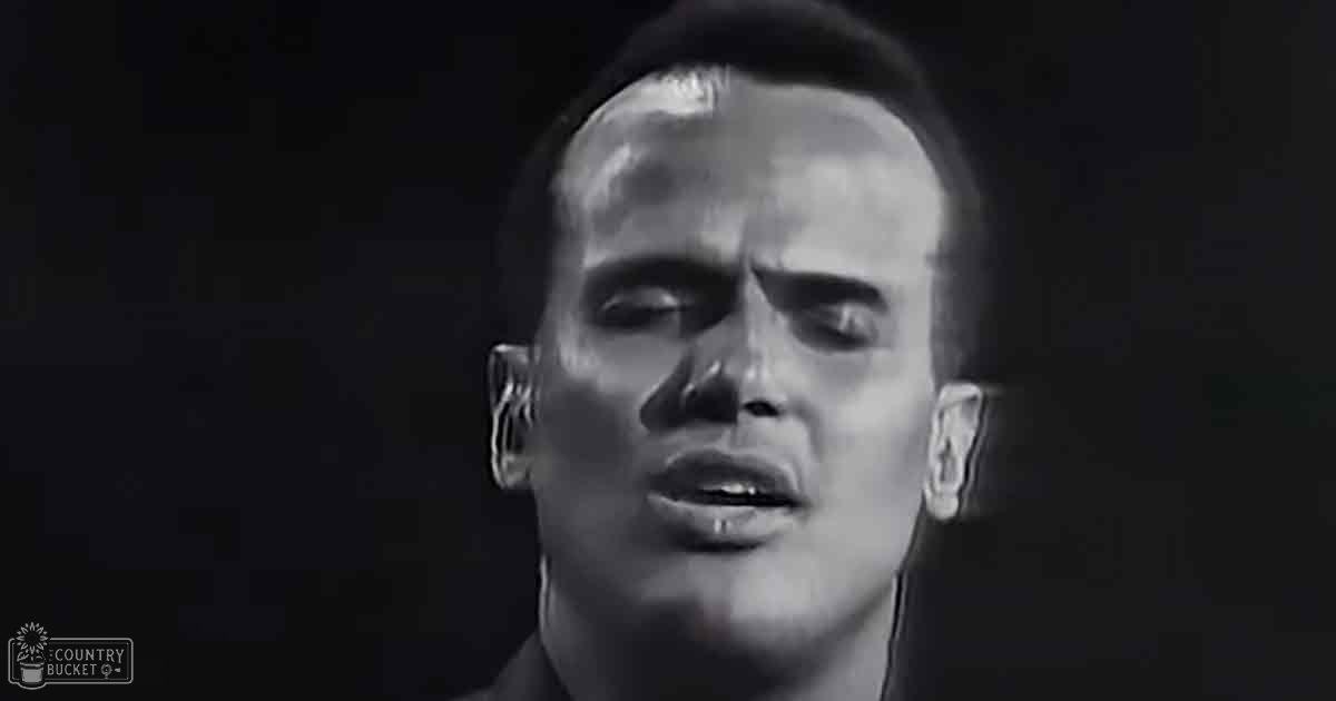 A young adult male wearing a dark-colored garment with a high collar indoors.