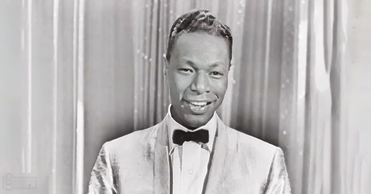Young adult male wearing a formal suit jacket with a bow tie, standing indoors against a curtain backdrop suggesting a stage or performance area.
