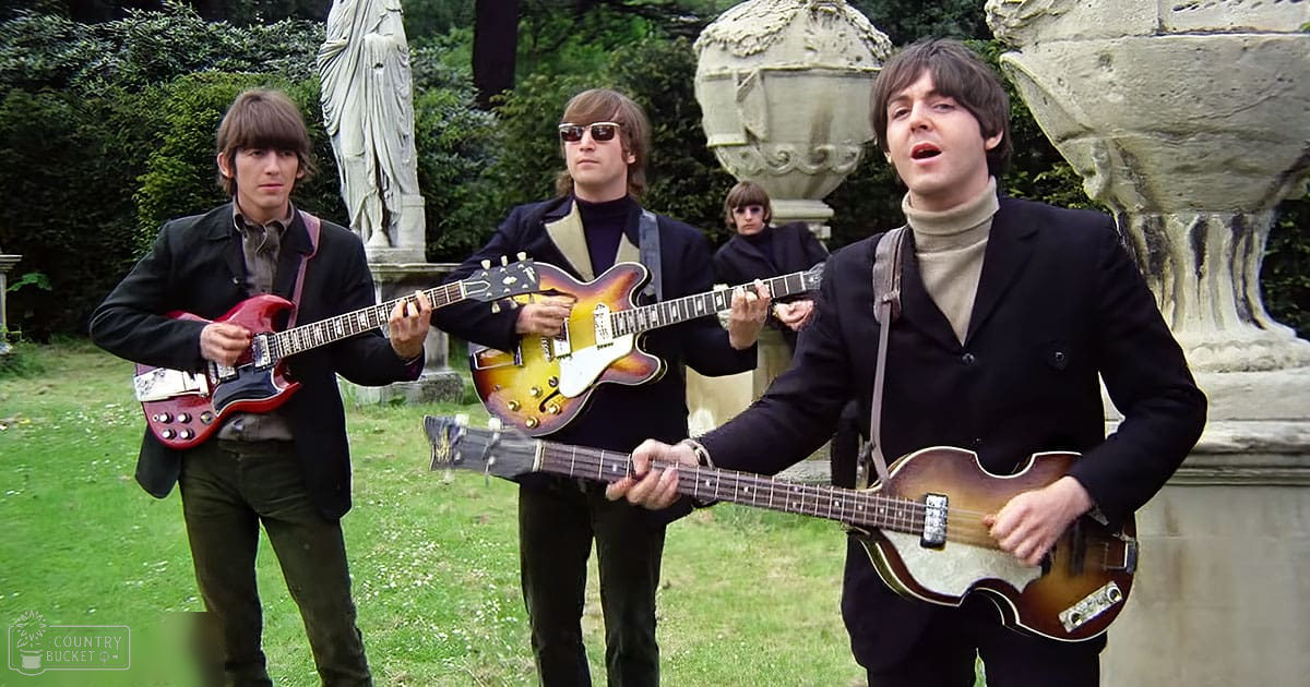 Outdoor garden scene with statues, young adult males performing music, green grass, brown statues, black jackets, beige shirts, daytime spring or summer light