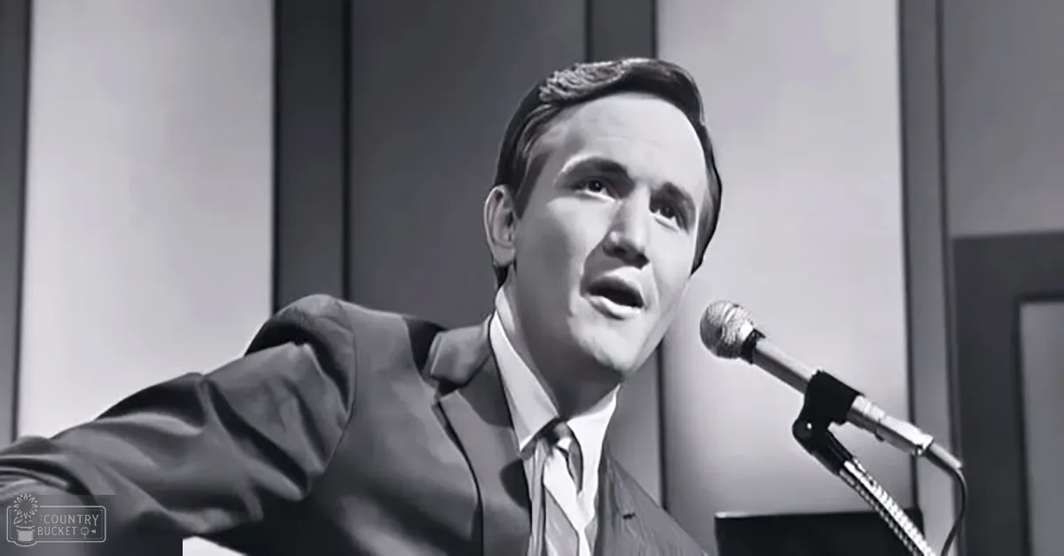 Young adult male in dark suit jacket, white dress shirt with tie, singing into microphone in studio setting.