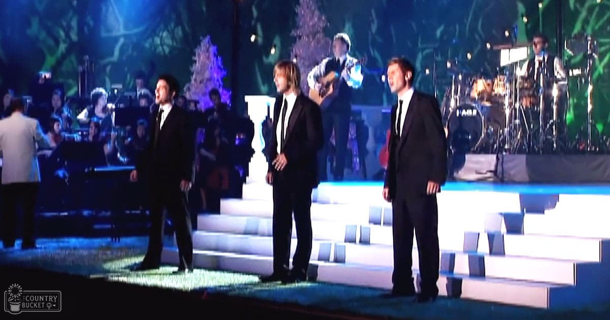 A musical performance scene indoors at an awards show or concert with stage lighting and performers in dark suits.