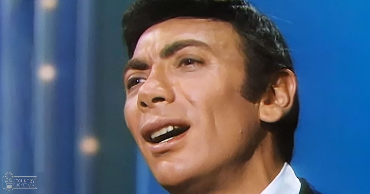 Young adult male in a fitted, tailored white shirt with a collar, mid-20th century style, indoors against a blue backdrop with vertical lines. 'Madly Odd' text printed bottom left.