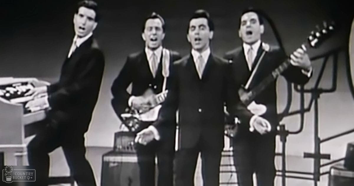 A mid-20th century musical performance scene with adults in dark suits holding electric guitars, set on an indoor stage lit for performance.