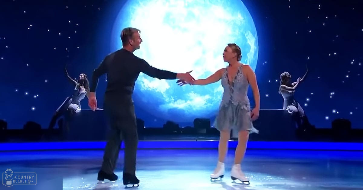 A couple ice skating in an indoor arena with a large illuminated moon and silhouettes of dancers in the background.
