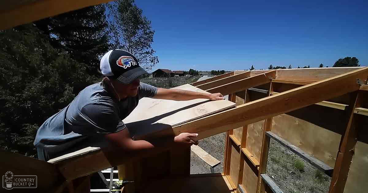 An adult male construction worker wearing a dark gray t-shirt with 'Arizona' text on his black and white baseball cap, working at an outdoor building site under clear blue skies in a suburban area.
