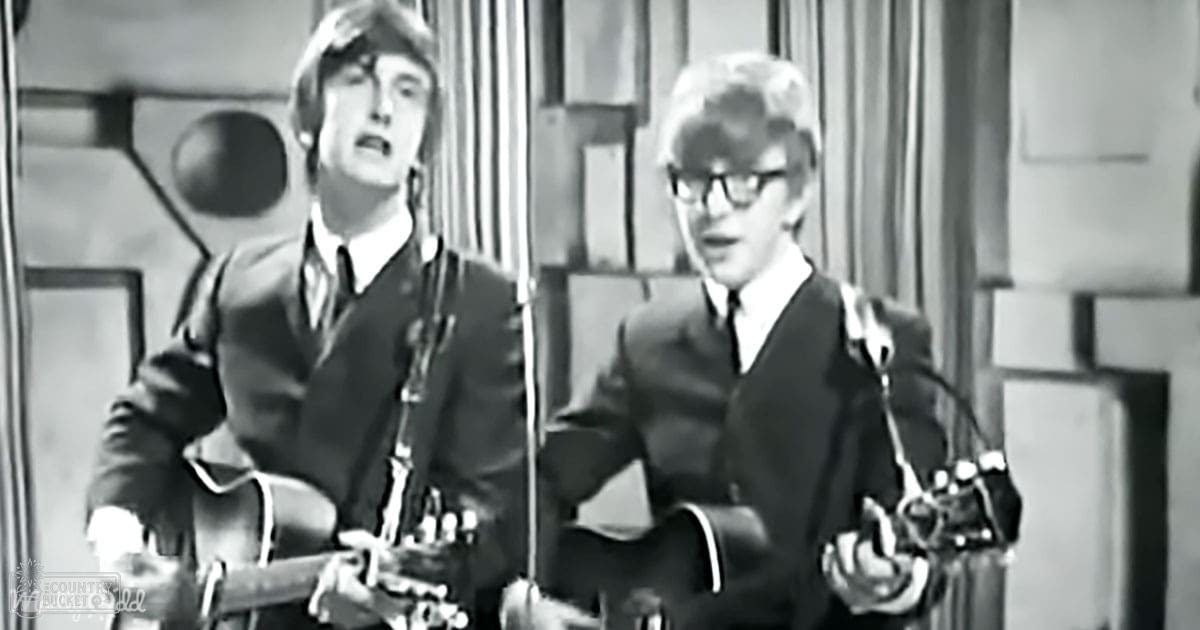 Musical performance scene with young adult males in formal suits on stage, microphone stands visible, even lighting, black and white image.
