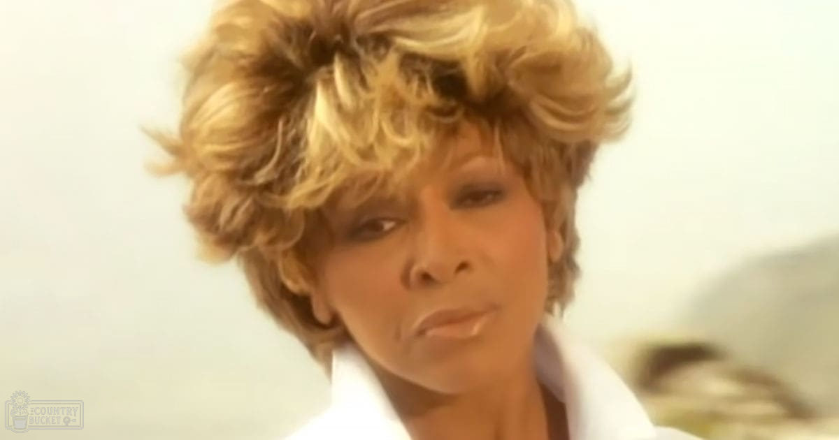 A middle-aged woman in a casual yet stylish white blouse with high collar indoors during daytime.