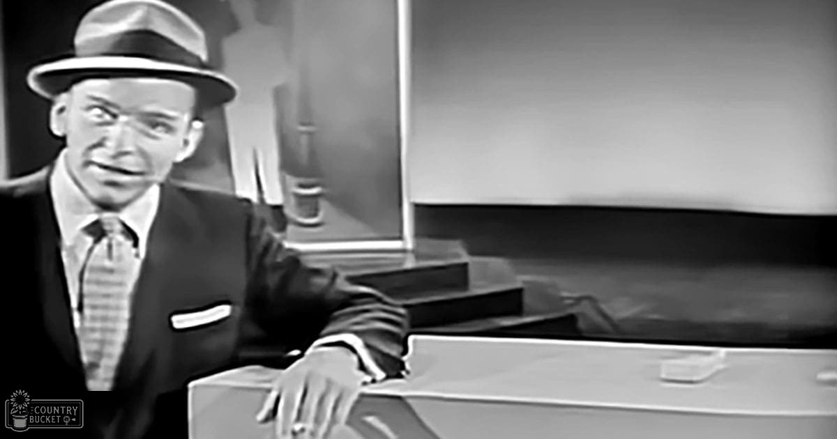 Adult male seated at a desk with dark suit jacket, striped tie, light-colored shirt. Indoors with artificial lighting.