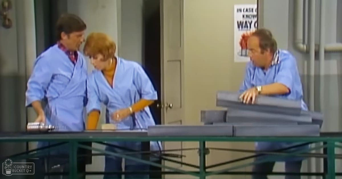 Medical or hospital setting with adults in surgical attire, glass table holding medical trays, indoor artificial lighting, light blue and white dominating the scene.