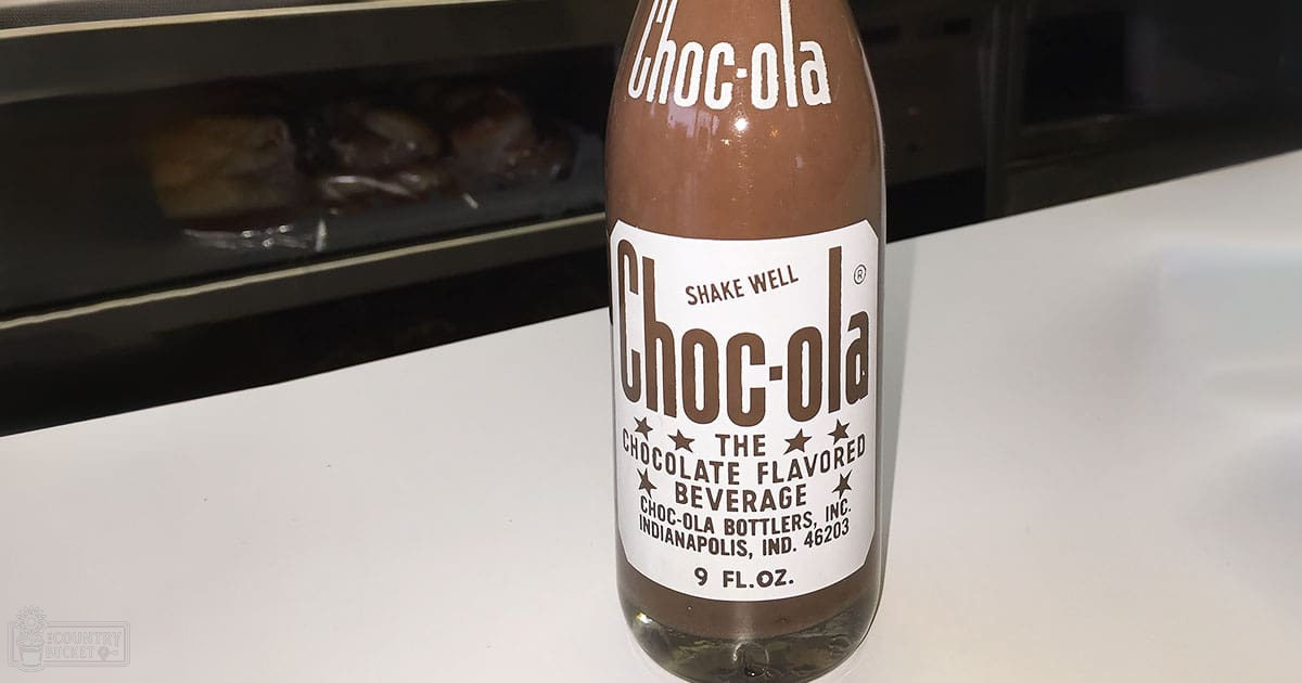 Close-up of a 'Choc-ola' chocolate-flavored beverage bottle on a white surface, indoors with artificial lighting.