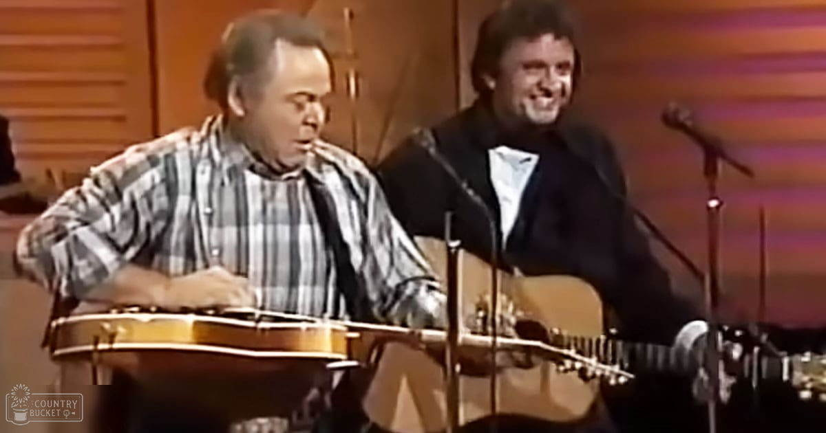 Musical performance in an indoor setting with wooden paneling, with two adult males dressed casually and formally.