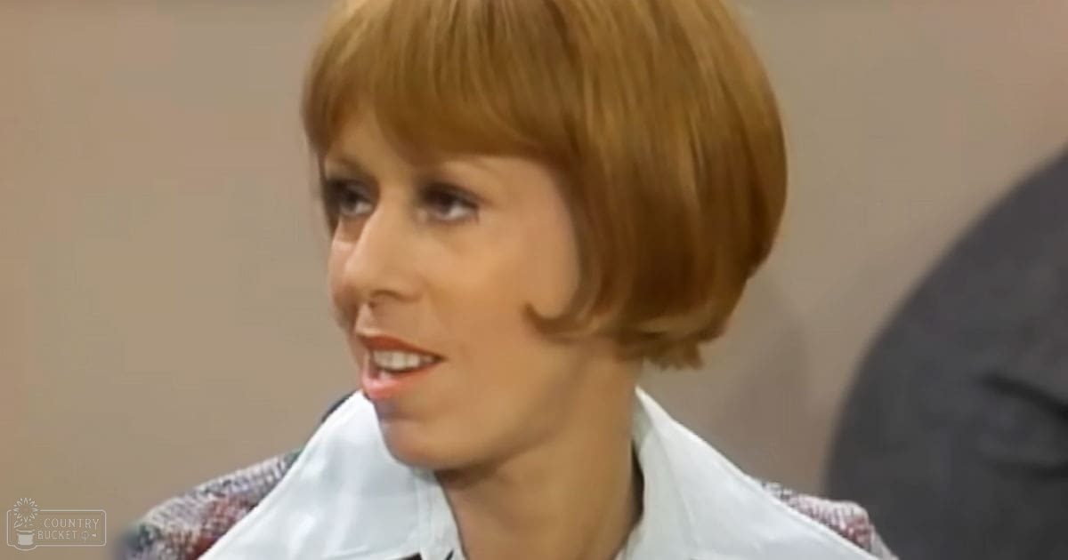 A middle-aged woman wearing a mid-20th century white shirt indoors with neutral-colored walls and even daytime lighting.