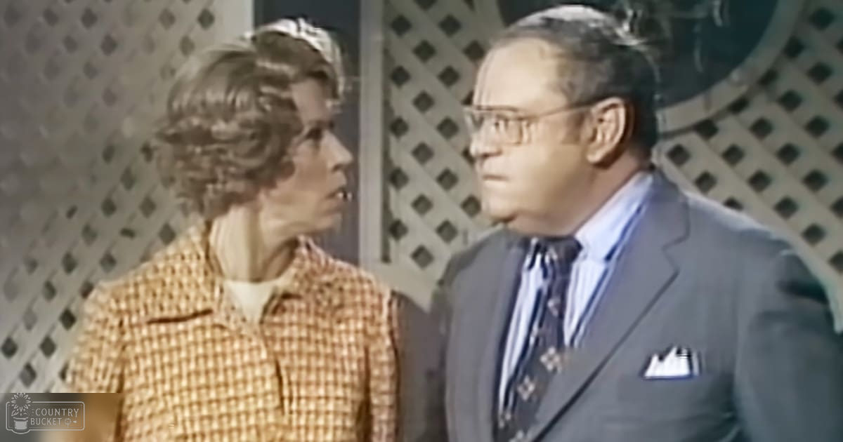 Middle-aged man in a formal setting with young adult female wearing checkered jacket, lattice pattern background, indoor scene with even artificial lighting.