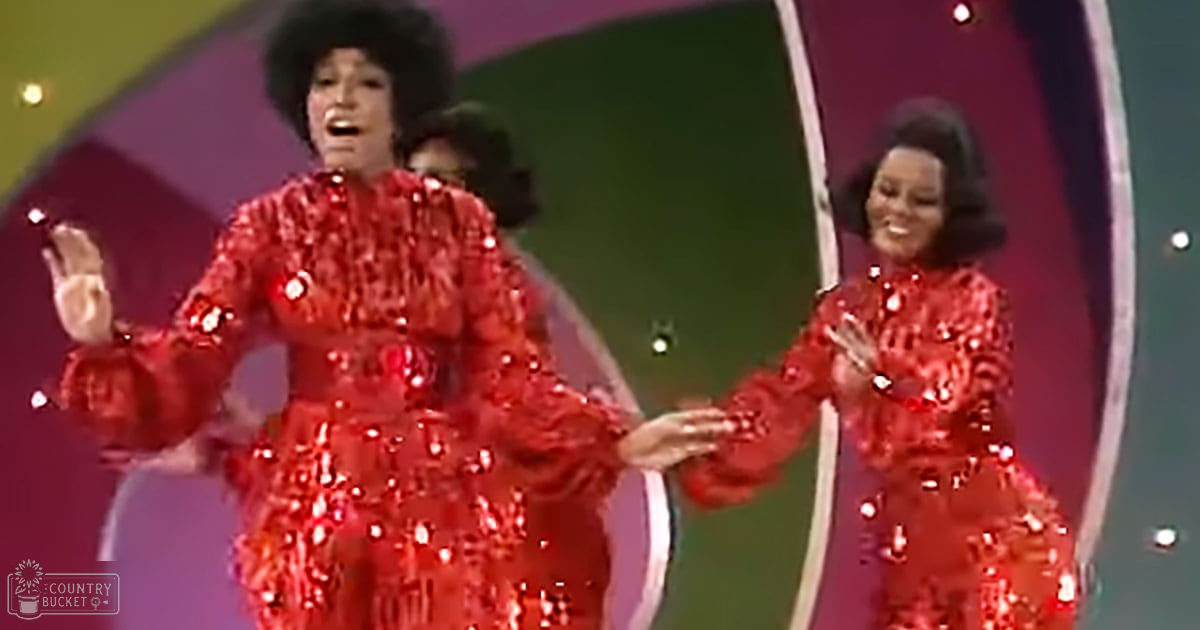 Adult female performers in red sequined dresses on a brightly lit stage with green and purple backdrops, likely from an entertainment venue.