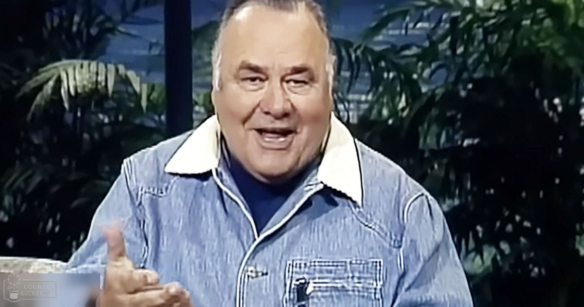 An older adult male wearing a denim jacket with white trim, blue shirt, set against a backdrop of tropical foliage and palm trees.