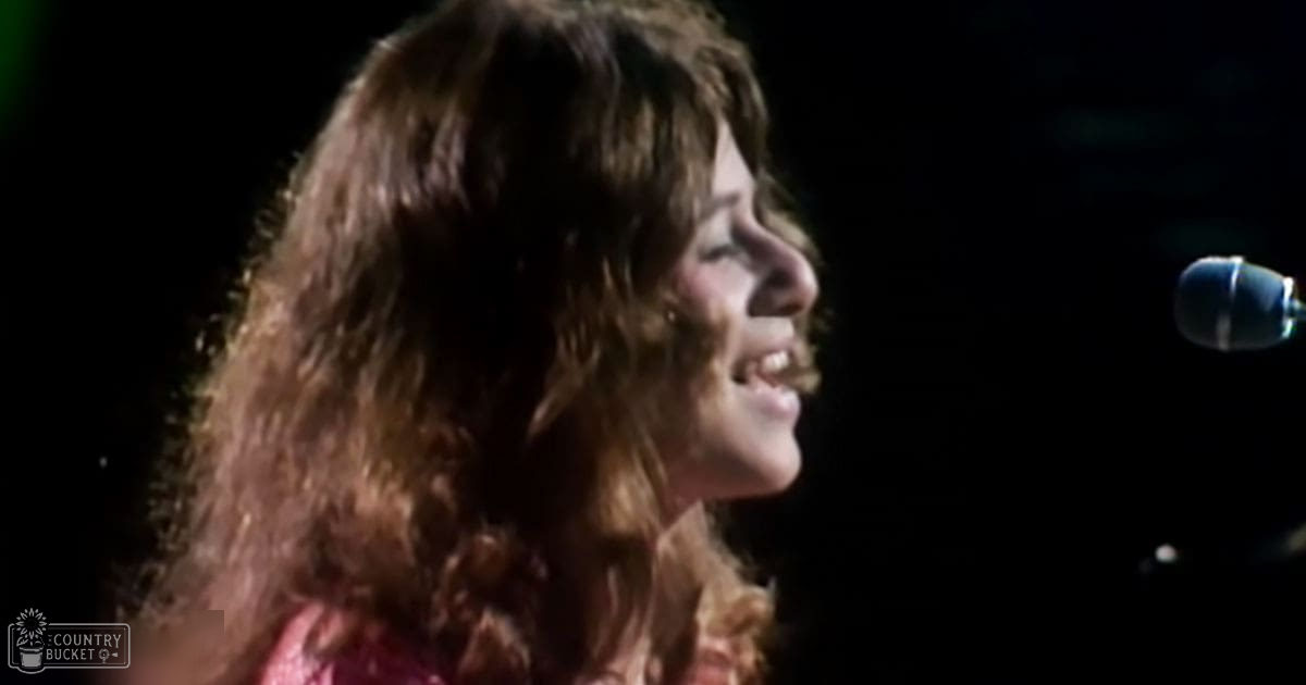A young adult female sings into a microphone at an indoor event under dim stage lighting.