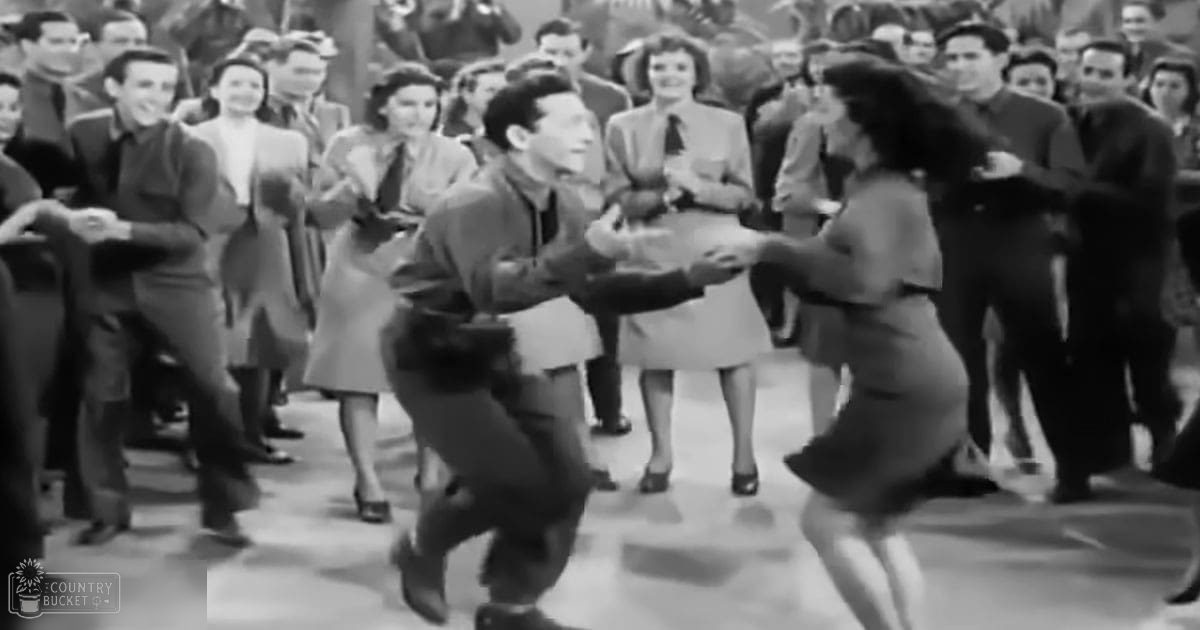A dance scene in an indoor setting with young adults dressed in formal attire from the 1940s-1950s, with spectators in suits and dresses, suggesting a social gathering or event.