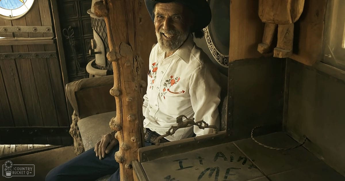 An older adult male in a rustic cabin setting, wearing a long-sleeved button-down shirt with an embroidered floral pattern inspired by cowboy attire from the late 19th century and blue jeans.
