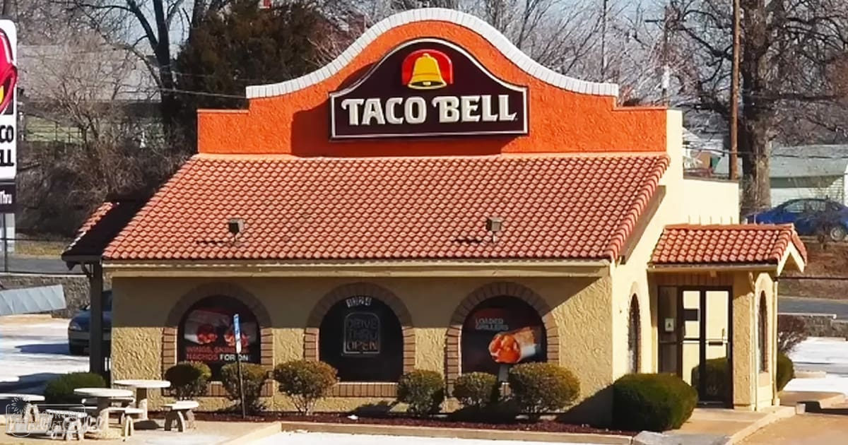 Taco Bell restaurant in an urban or suburban area with outdoor seating and a 'Drive Thru Open' sign.
