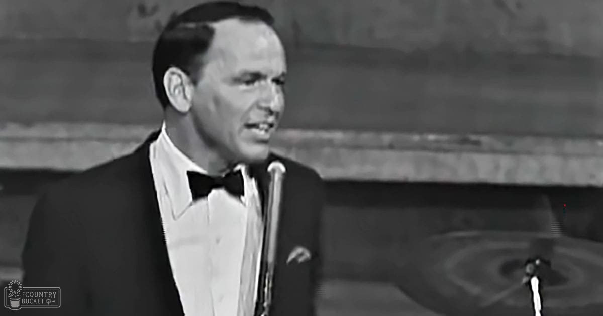 Adult male singer wearing a formal tuxedo with bow tie on stage; indoor setting with blurred backdrop suggesting performance venue.