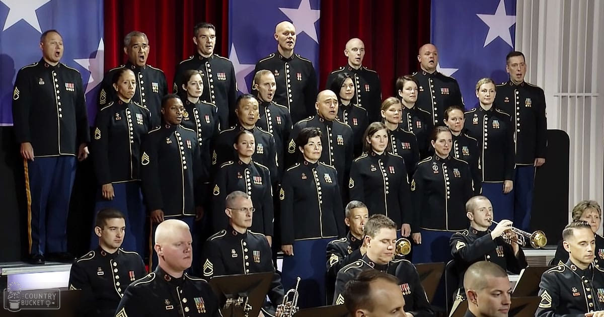 Adult males in dark blue wool uniforms with gold trim and medals perform indoors. Red curtains serve as a backdrop.