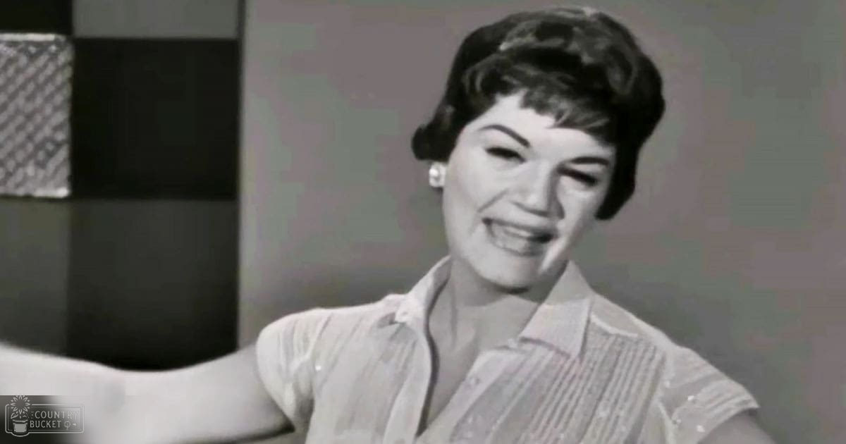 An adult female wearing a light-colored, horizontally striped blouse with short sleeves and a collared neckline, seated indoors under artificial lighting.