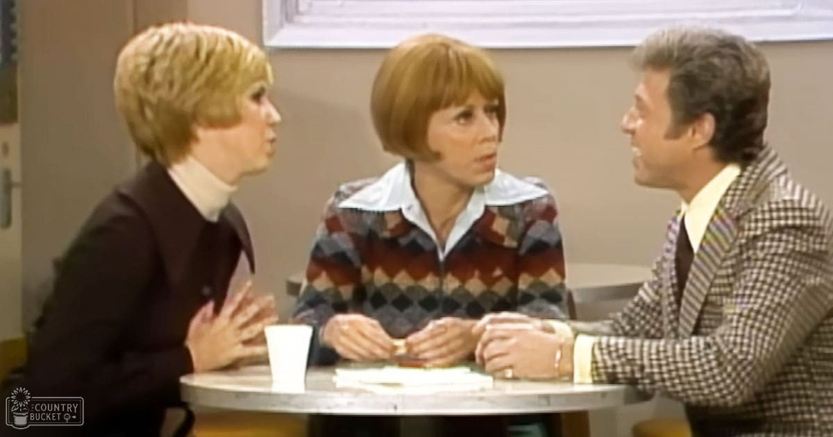 Three adults engaged in a group discussion within an indoor studio or office setting, with neutral-toned walls and professional furniture.
