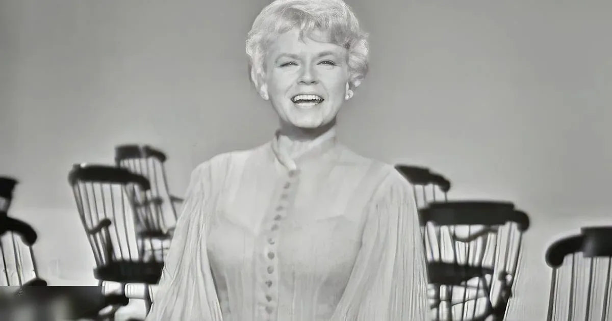 Middle-aged woman wearing a loose, vintage-style long-sleeved blouse indoors with classic chairs and even lighting.