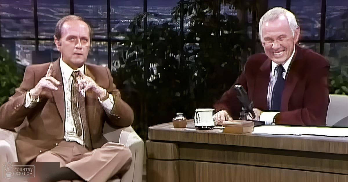 A talk show host seated behind a desk with another individual gesturing animatedly, suggesting an engaging conversation in a television studio setting at night.