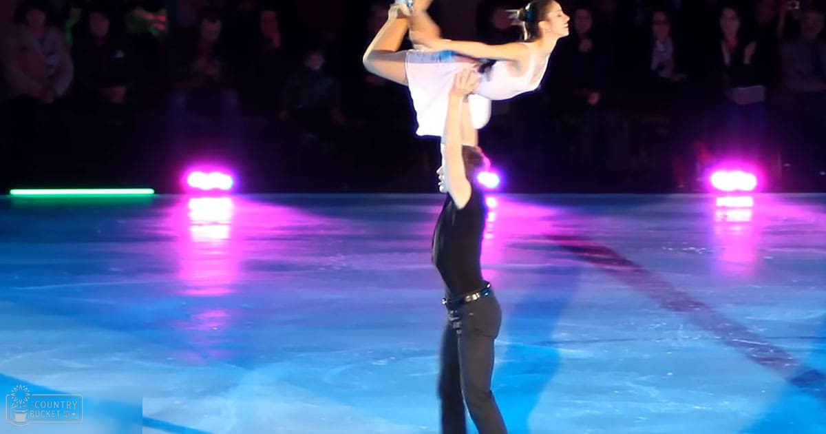 A figure skating pair performing on an ice rink with a purple and green lit audience in the background.
