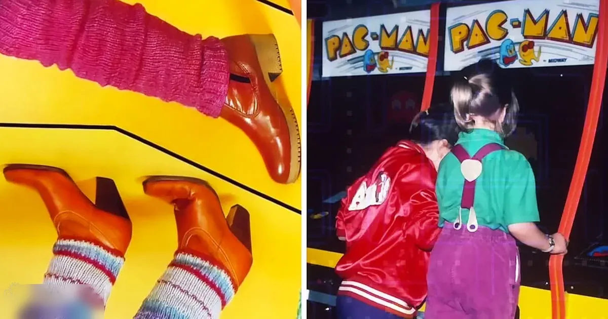 A child wearing a red jacket and green shirt plays PAC-MAN in an indoor arcade with another child, both holding handles attached to the arcade machine.