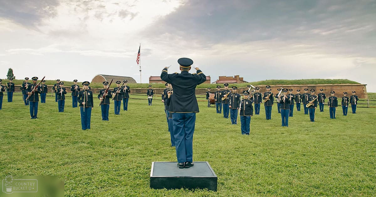 A military band practicing outdoors at Fort McHenry in Baltimore, Maryland with partly cloudy skies and grassy terrain.