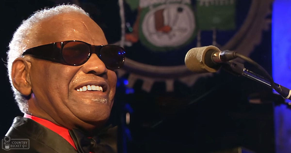 Older adult male singing at a music event with microphone; indoor venue with dim lighting and colorful backdrop