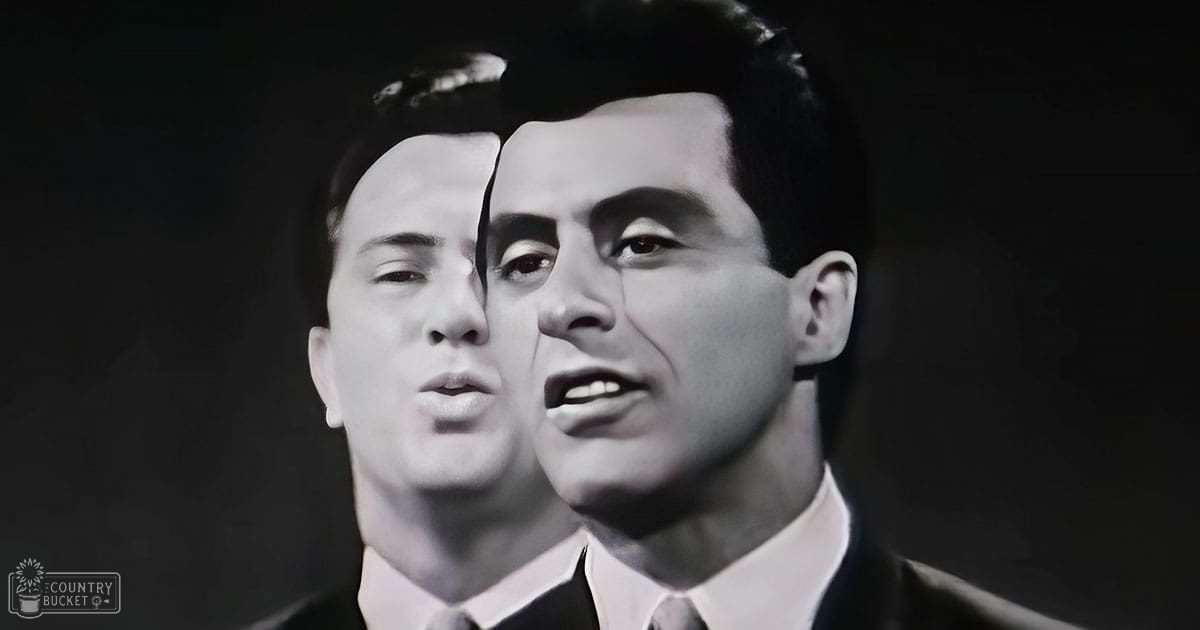 Two adult males in formal attire, classic mid-20th century suits with white shirts and ties, 'Madly Odd' text on garment, dark indoor setting with artificial lighting.