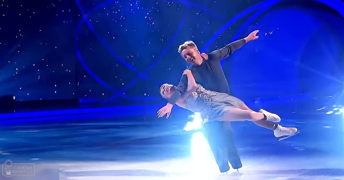 A figure skating couple performing on an ice rink under a starry backdrop at night.