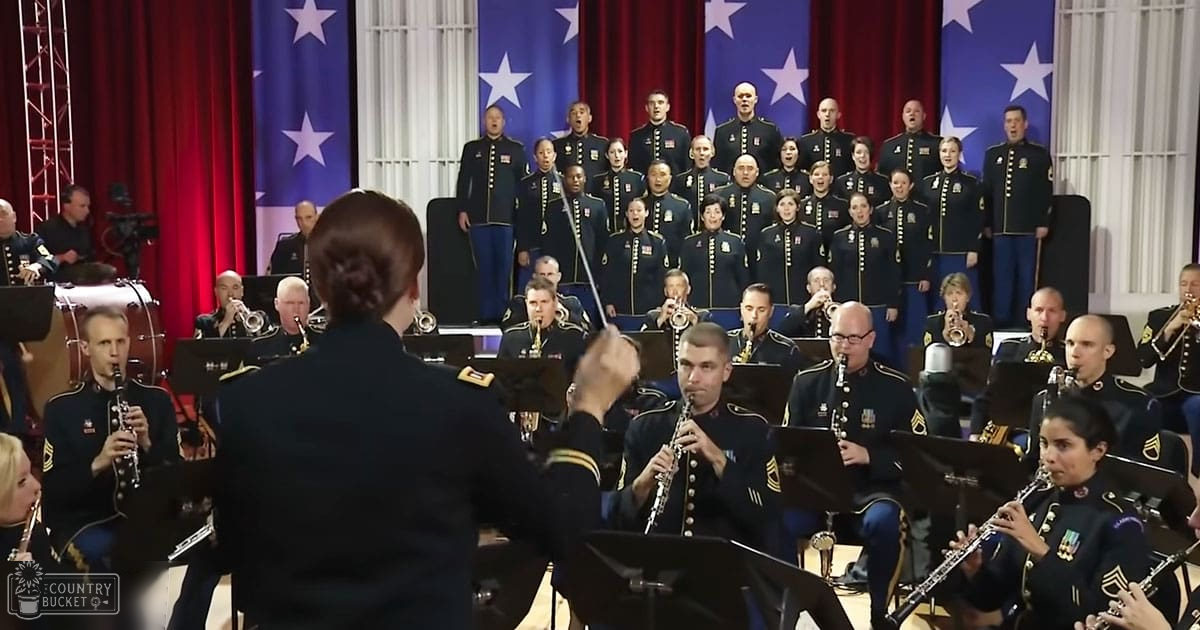 A military band performing indoors at a formal event with red curtains, American flags, musical instruments, and sheet music.
