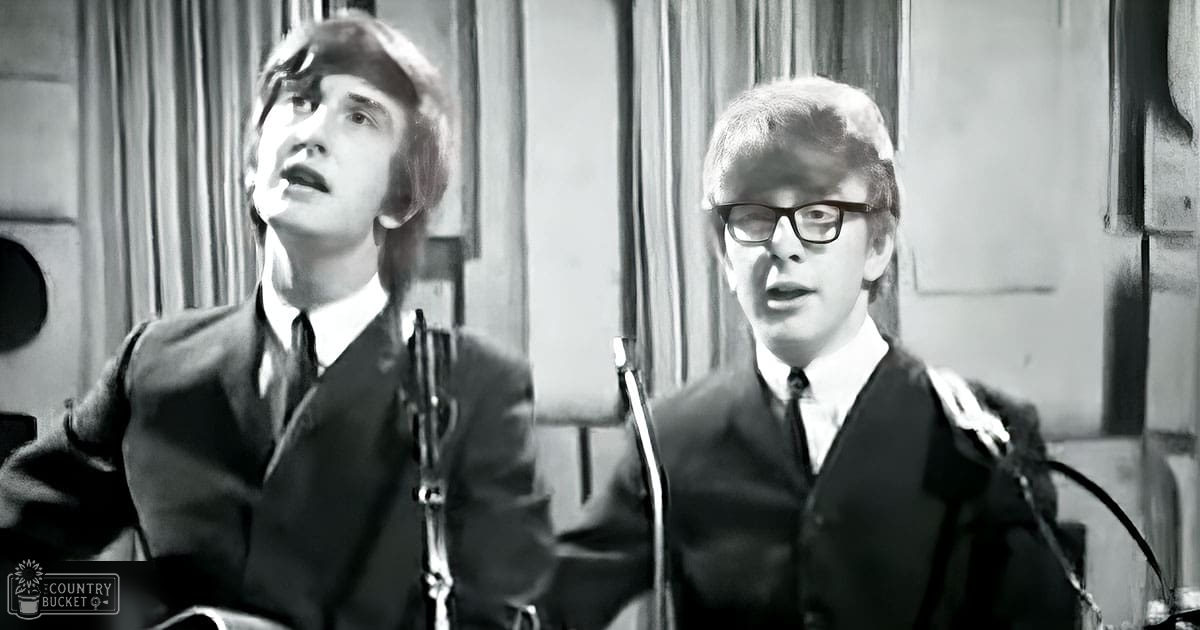 Two young adult males wearing dark suits and white shirts with microphones in front of them in an indoor studio setting.