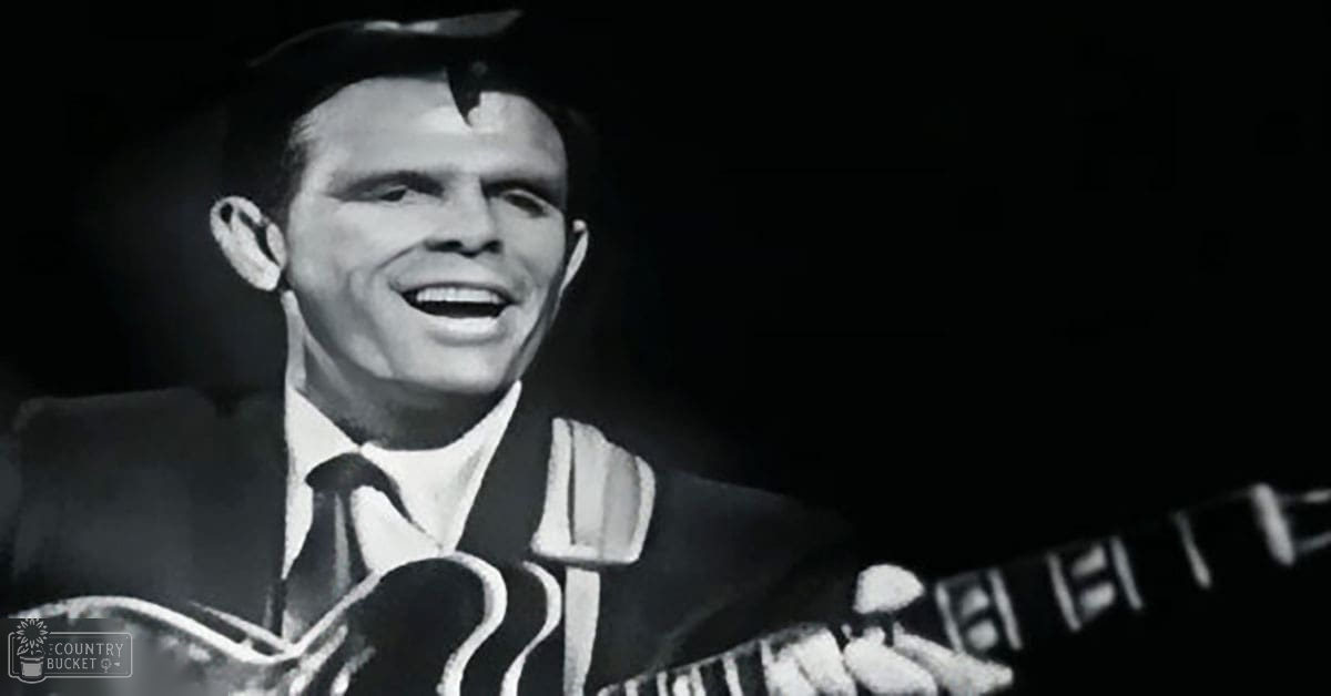 Adult male performer in dark suit with striped tie, holding microphone on indoor stage; black and white attire contrasts against blurred dark backdrop